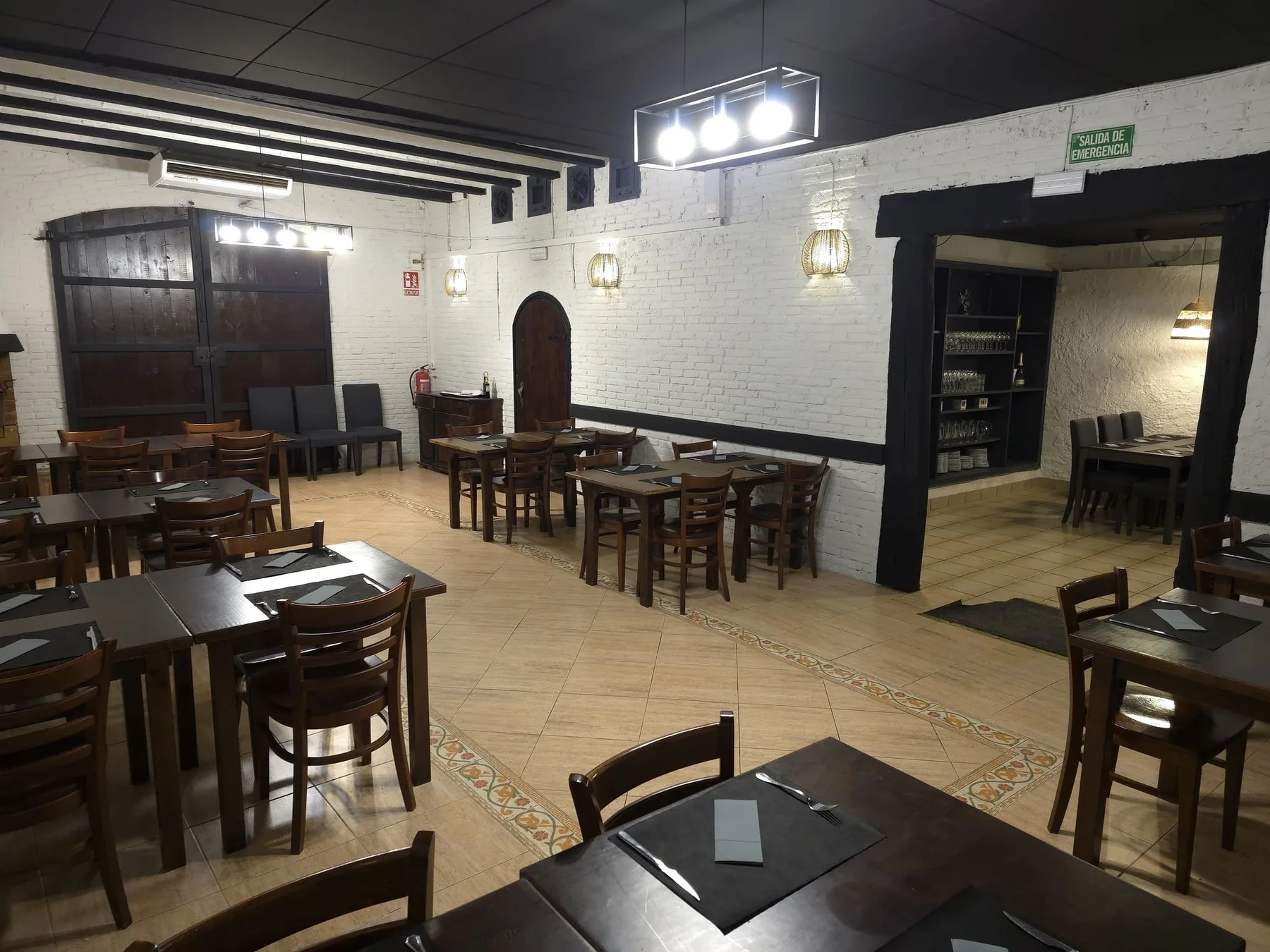 La sala gran de Kasolà: parets de maó blanc, bigues fosques, una gran porta antiga de fusta, una porta d'arc i taules de fusta parades